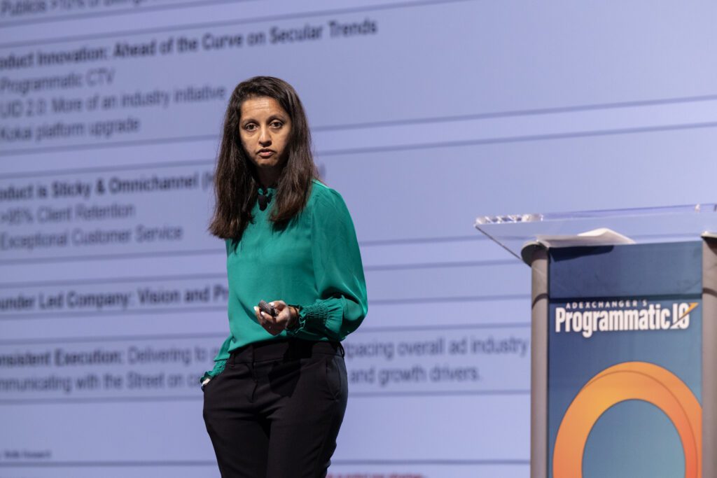 Shweta Khajuria, Managing Director of Wolfe Research standing on stage with a green shirt next to the Programmatic IO podium.